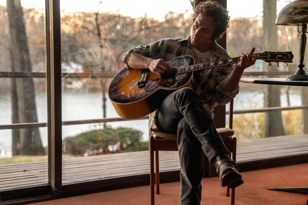 Here's A Show And Movie You Need To Watch This Weekend, Plus More TV And Movie News You Might've Missed 15 Person indoors playing an acoustic guitar, sitting cross-legged on a chair, with a forested outdoor scene visible through large windows