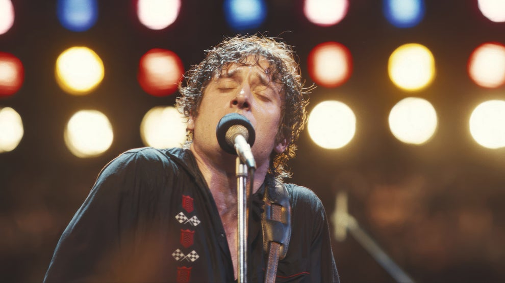 Here's A Show And Movie You Need To Watch This Weekend, Plus More TV And Movie News You Might've Missed 11 Musician passionately singing on stage with eyes closed, holding a guitar. Bright lights shine in the background, creating a vibrant atmosphere