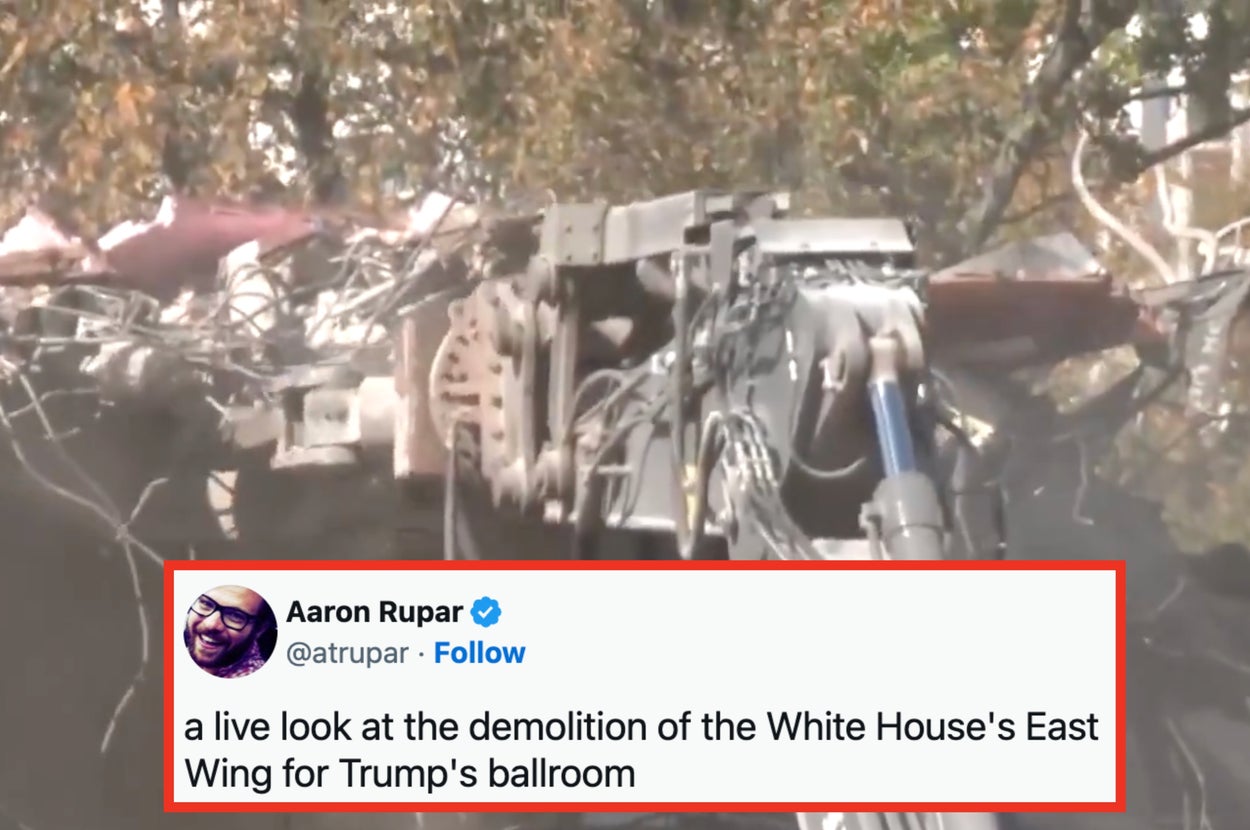 Excavator demolishing a building, with debris and exposed wires visible, during a construction site operation