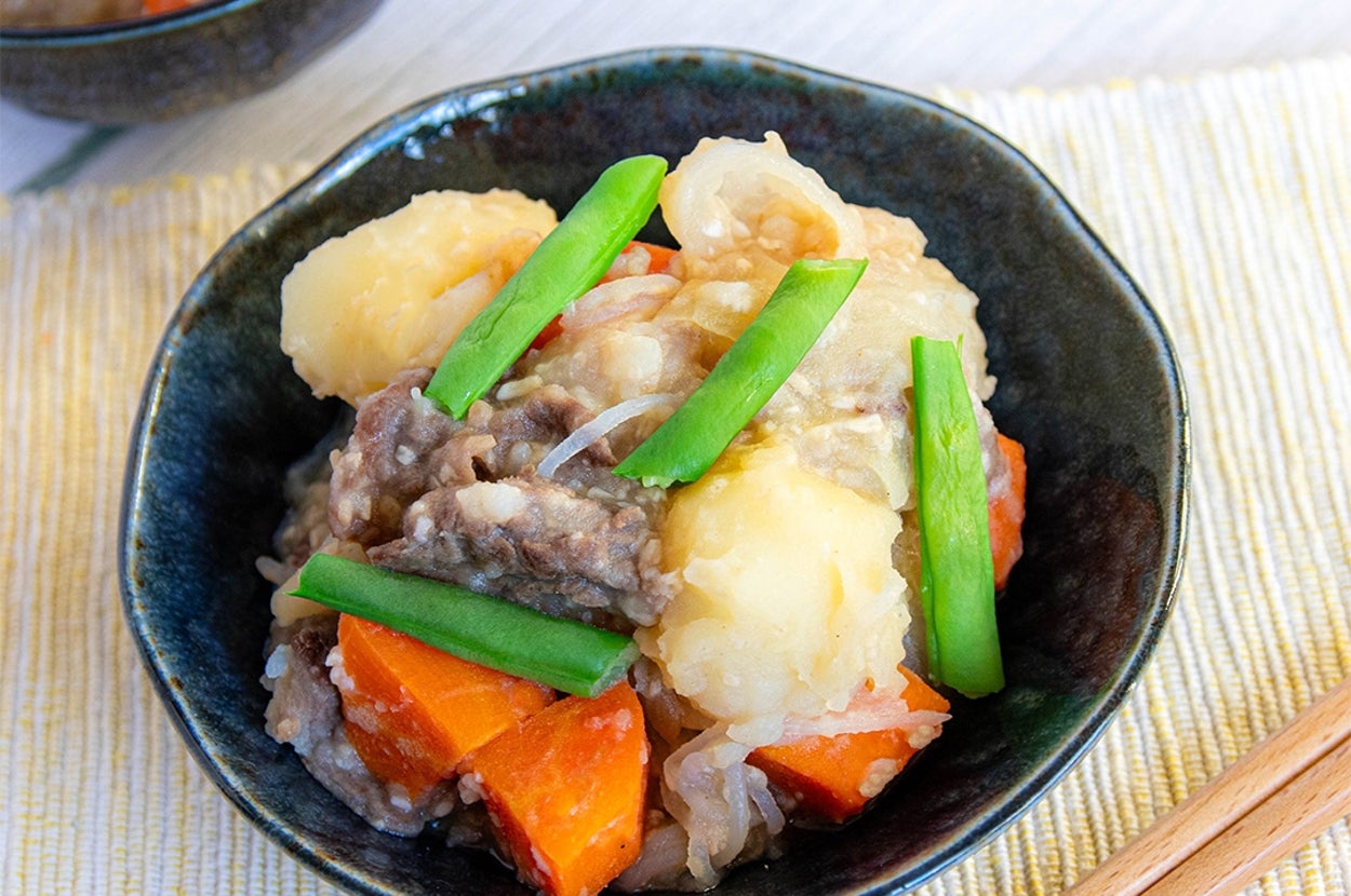 肉じゃがの料理。じゃがいも、にんじん、インゲンと一緒に牛肉が黒い器に盛られている。
