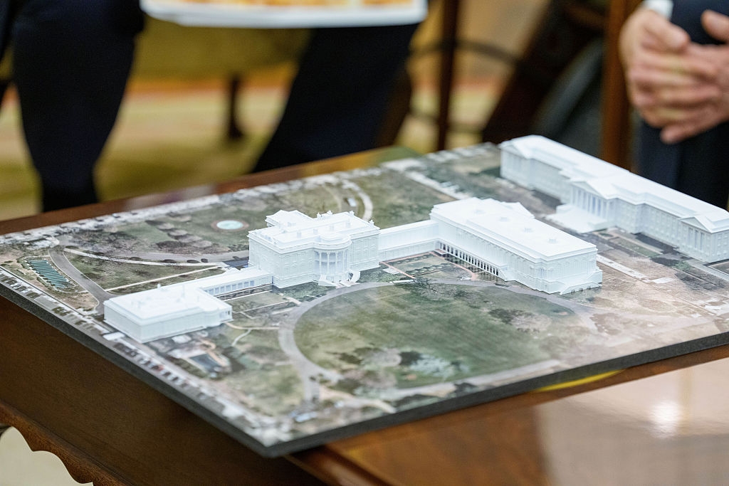 Architectural model of a large building complex on a table, surrounded by people observing