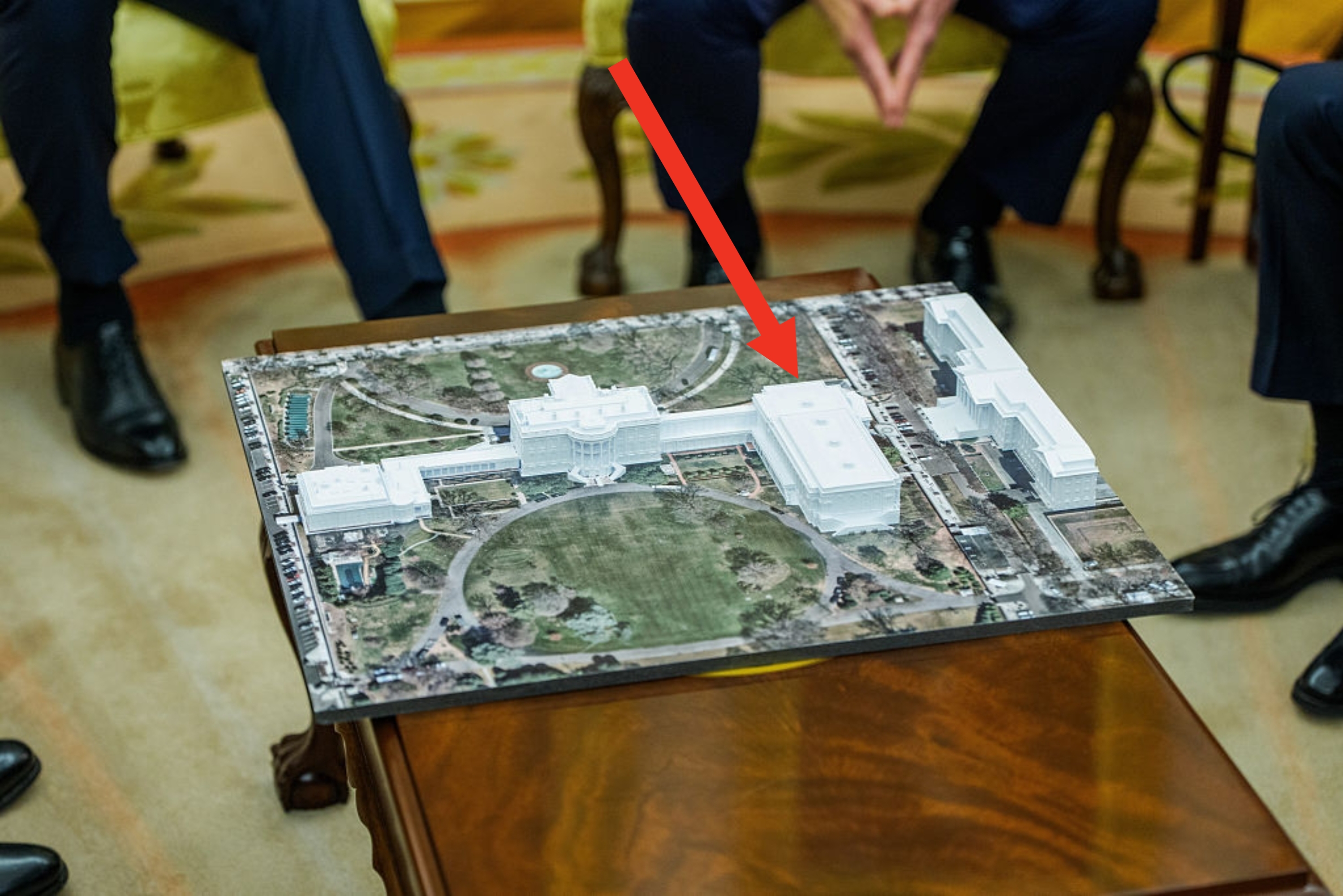 People seated around a table with a detailed aerial photo of a large building and gardens