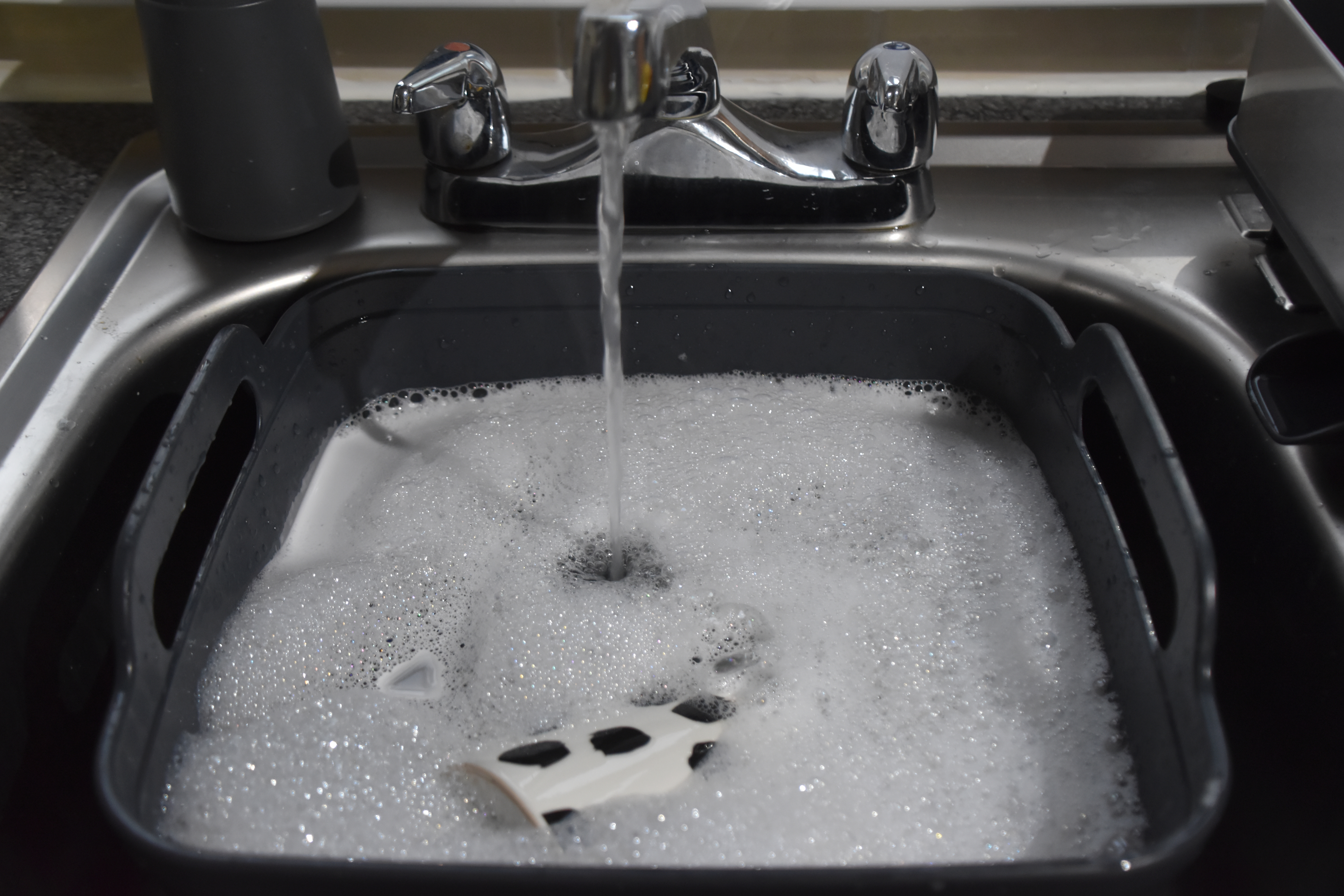 Oppvaskmaskin bestikkurv bløtlegging i såpevann i en kjøkkenvask med rennende kran