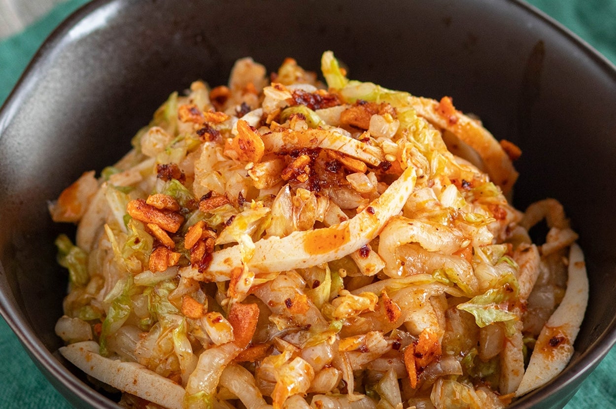 キャベツや野菜を炒めた料理が黒いボウルに盛られた画像。料理の上にはサクサクしたトッピングが施されている。