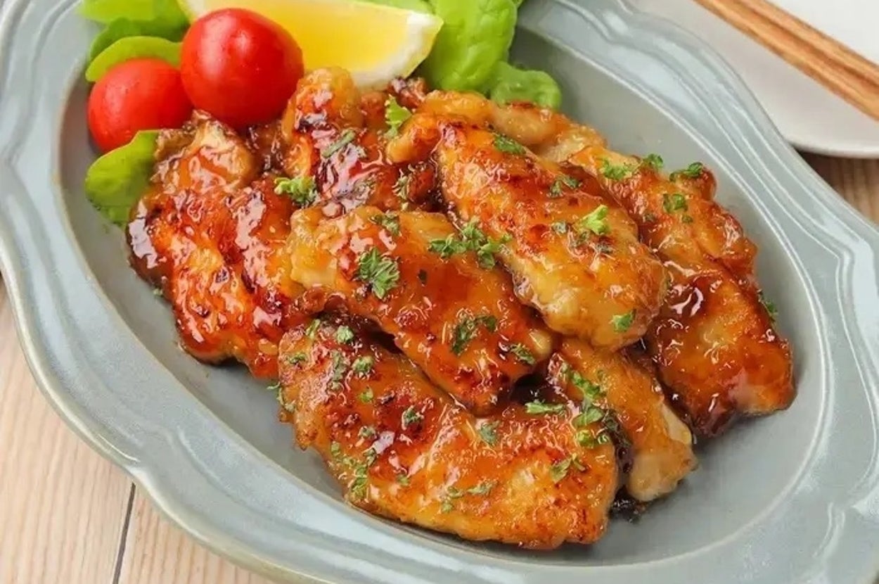 セラミック皿に盛られた鶏の照り焼き、レタス、ミニトマト、レモン添え。箸と小皿が横にあります。