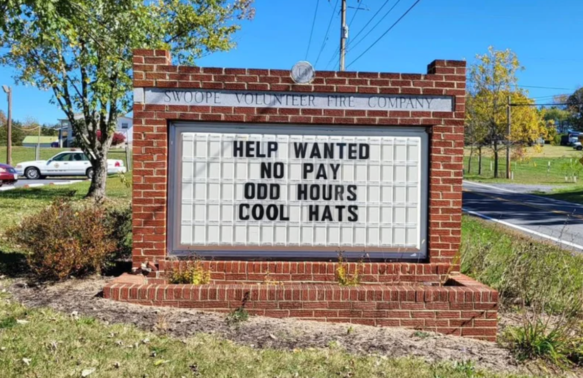 Sign at Swope Volunteer Fire Company reads: "Help wanted. No pay. Odd hours. Cool hats."