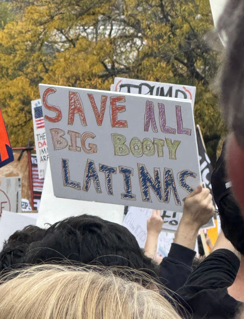 Crowd at a protest holds a sign reading "Save All Big Booty Latinas."