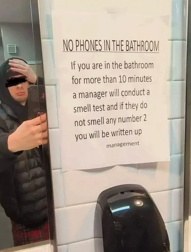 A sign in a bathroom warns employees against phone use, stating managers will conduct a smell test and possibly issue a write-up after 10 minutes