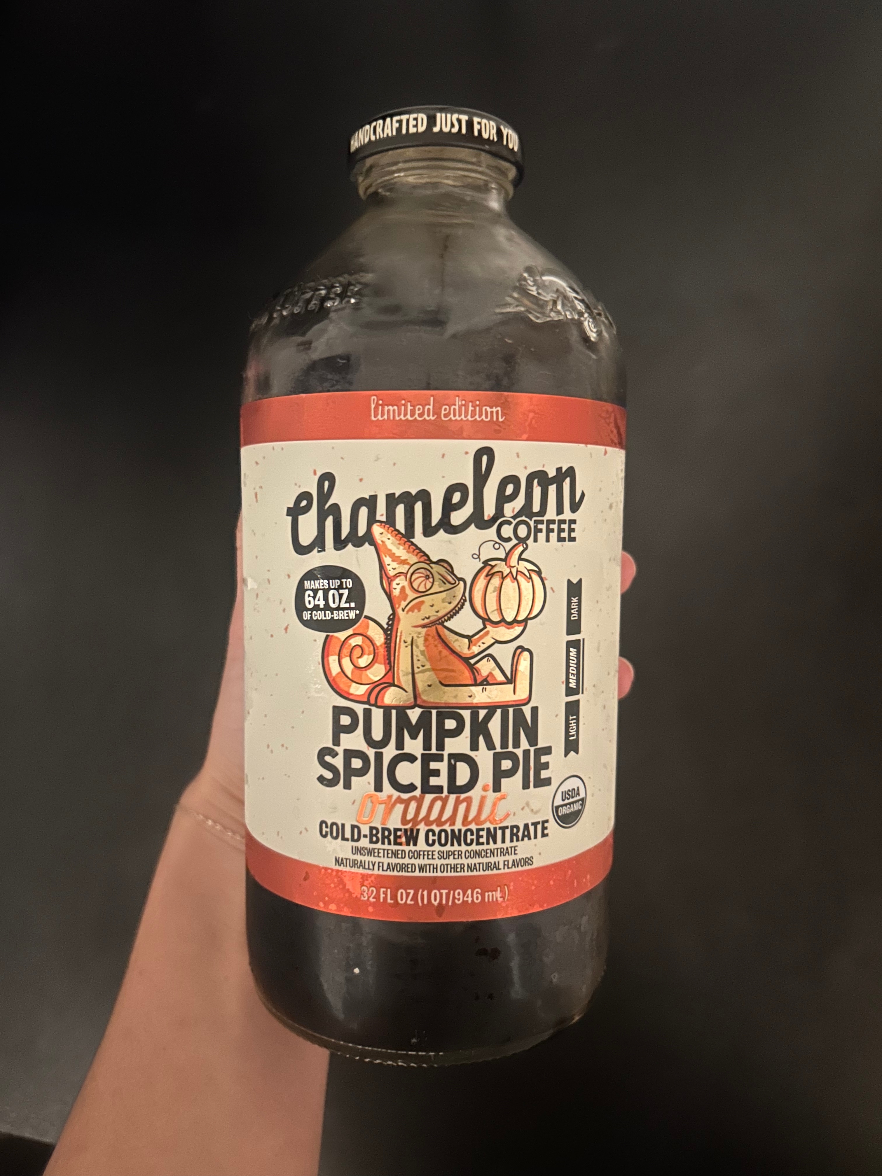 A hand holds a 32 fl oz bottle of Chameleon Organic Pumpkin Spiced Pie Cold Brew Coffee Concentrate