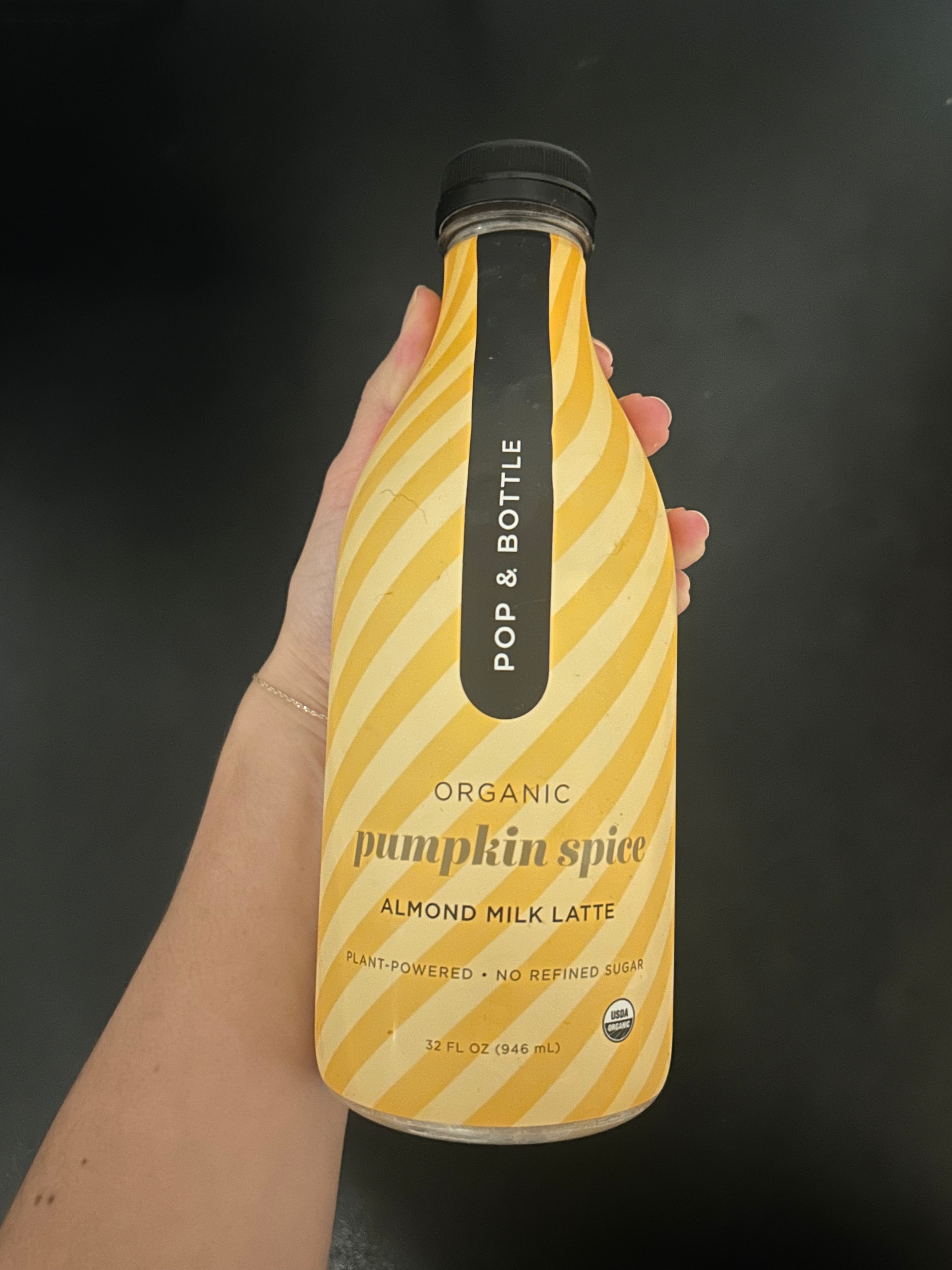 Hand holding a bottle of Pop &amp;amp; Bottle organic pumpkin spice almond milk latte, plant-powered, with no refined sugar