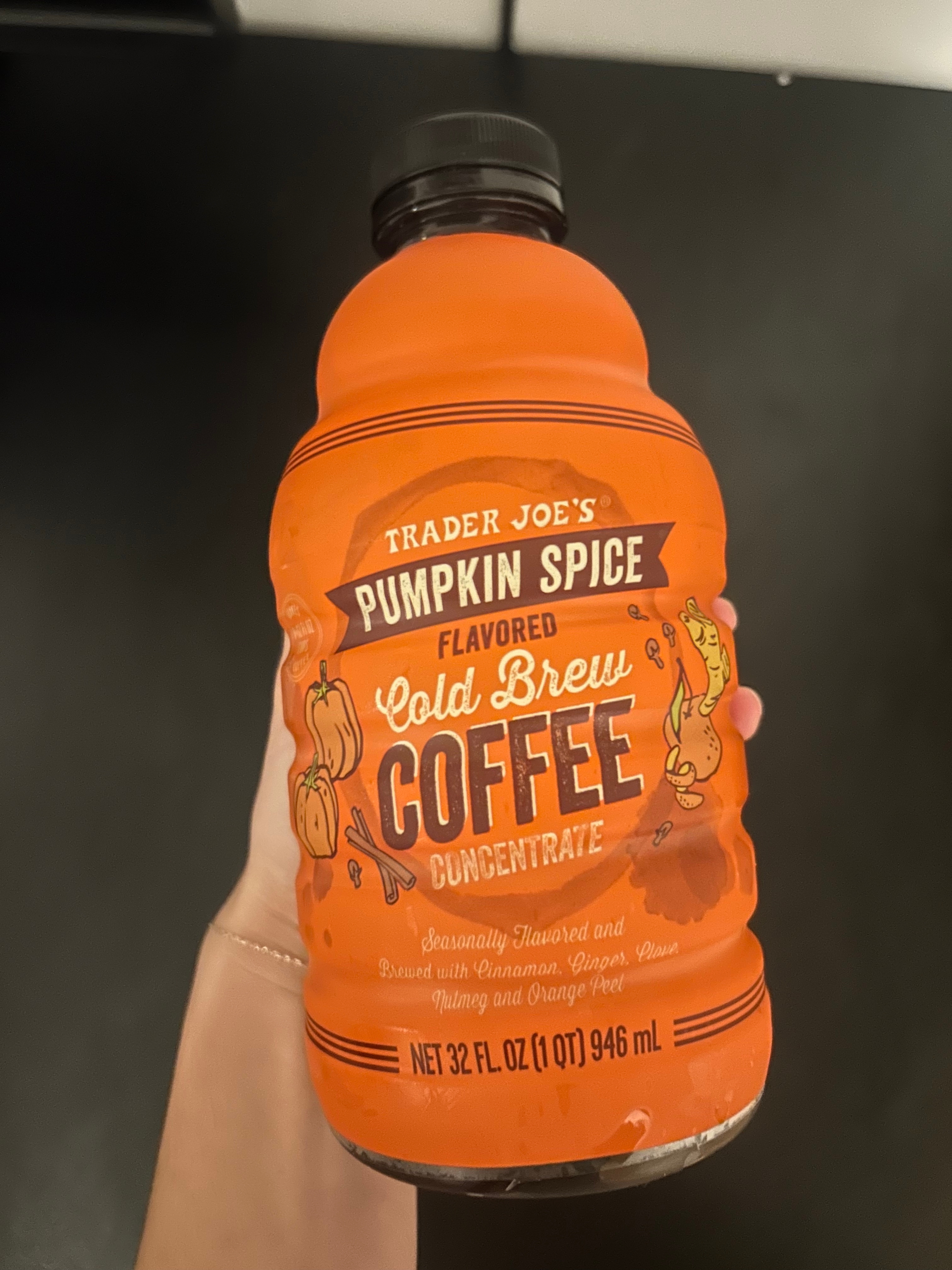 A hand holds a bottle of Trader Joe&#x27;s Pumpkin Spice Cold Brew Coffee Concentrate, labeled with fall-themed imagery