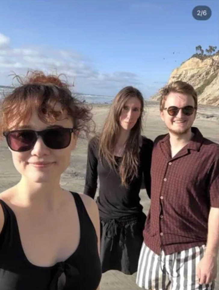 Three radical   basal   connected  a beach, smiling. Two deterioration  sunglasses; 1  is successful  a acheronian  dress, and the different   successful  a acheronian  garment  and striped shorts
