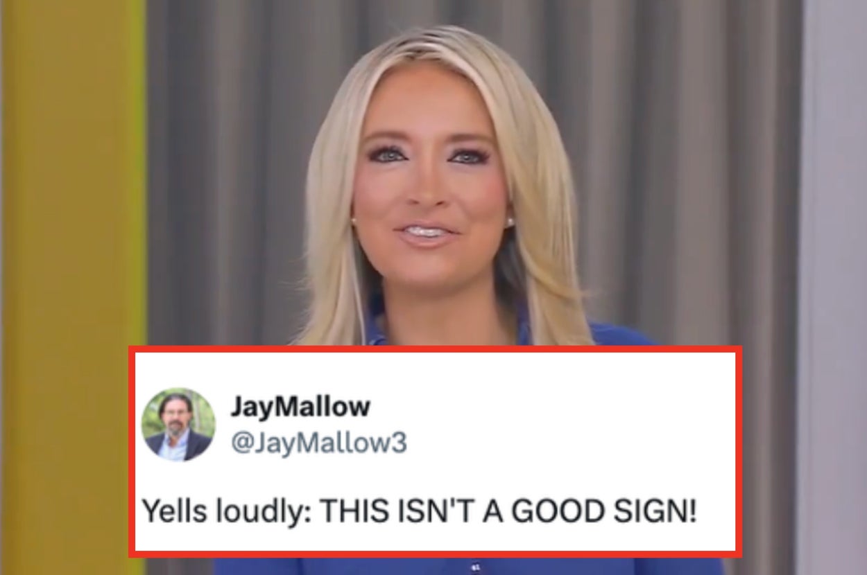 Person with long hair in a blue dress speaks in front of a news studio backdrop on live television