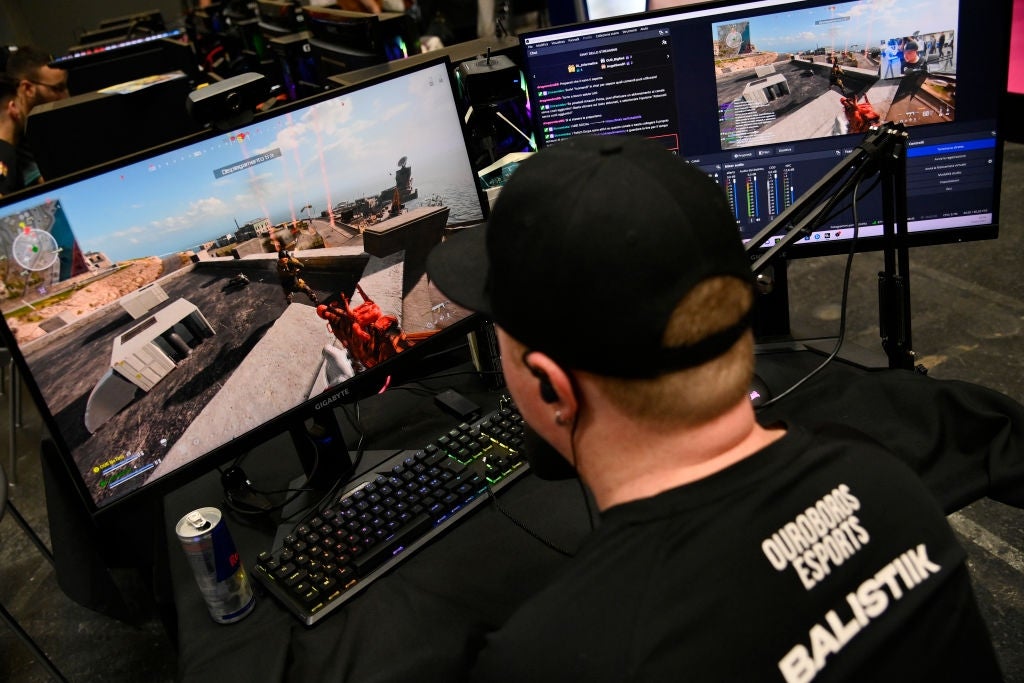 Person streaming a video crippled  connected  2  monitors, wearing a headdress  and esports jersey, sitting astatine  a gaming setup