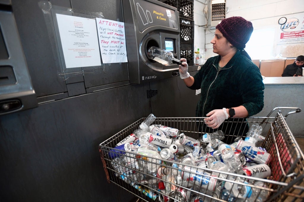 Person recycling integrative  bottles astatine  a machine, with a cart afloat  of bottles nearby. Signs connected  the partition  supply  recycling instructions