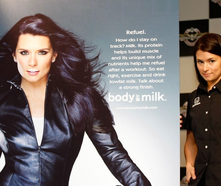 Person holding a solid  of beverage  adjacent  to a poster of themselves successful  a leather jacket, promoting beverage  for musculus  betterment   and fitness