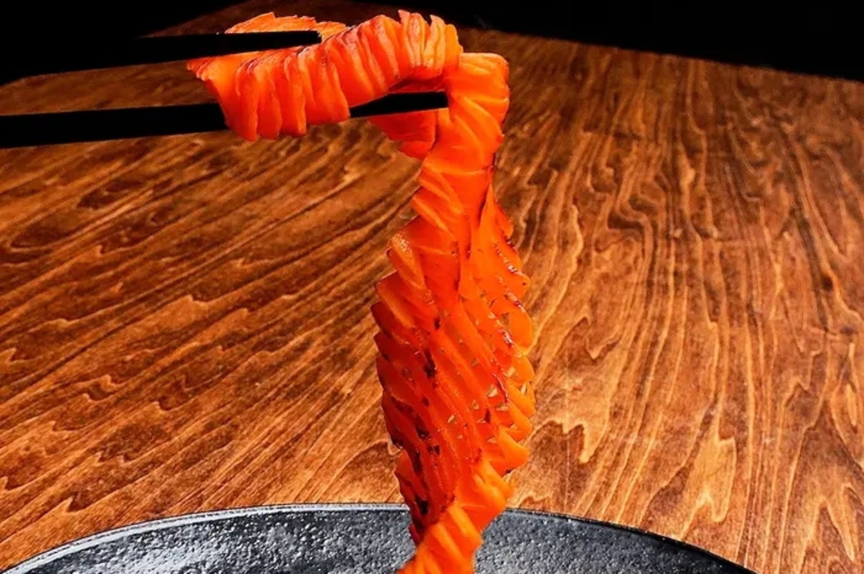 細かく切られたにんじんが立体的に盛り付けられている、黒い皿の上の料理。