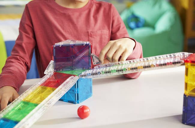 Child playing with a magnetic gathering acceptable connected a table, assembling colorful translucent geometric pieces into a structure