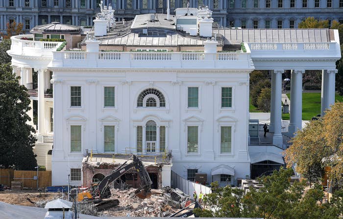 A construction scene showing demolition work in progress at the White House, with debris and equipment visible in front of the historic building