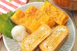 お皿に盛られた卵焼き2種類と大根おろし、葉が添えられている。背景に味噌汁。