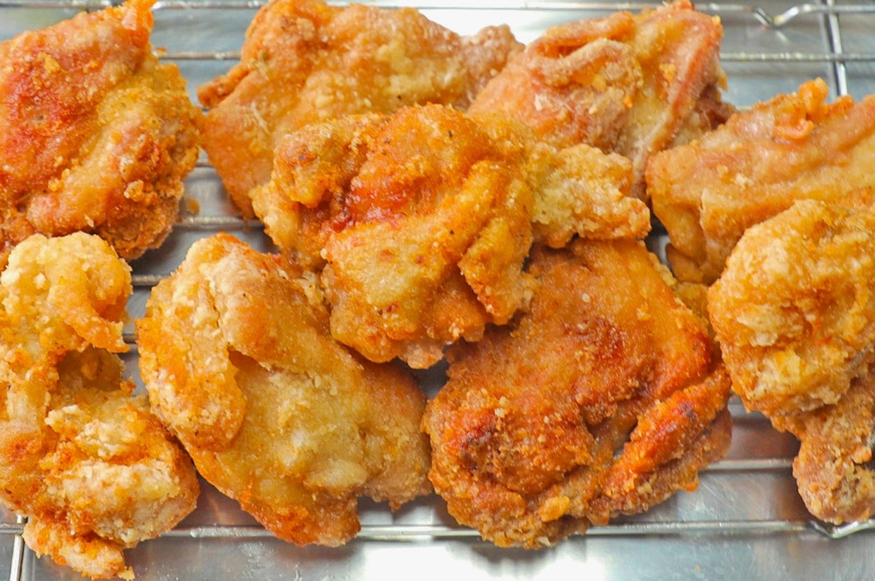 揚げられた唐揚げがラックに並べられ、そばにはサラダが添えられた皿があります。