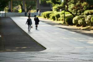 歩道を歩く制服姿の学生たち。背景には緑の植栽と他の歩行者が見える。
