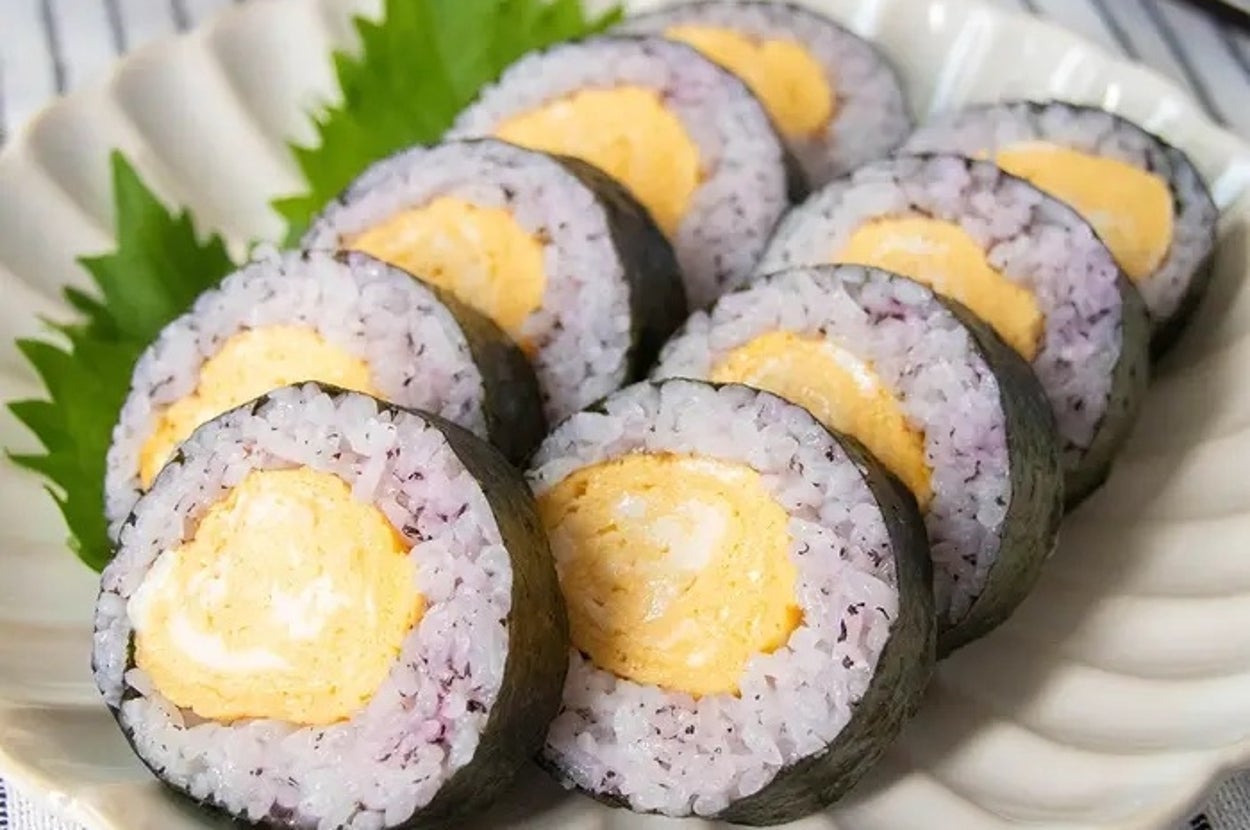 お皿に盛られた卵巻きの寿司が整然と並んでいる。後ろに箸と葉が添えられている。