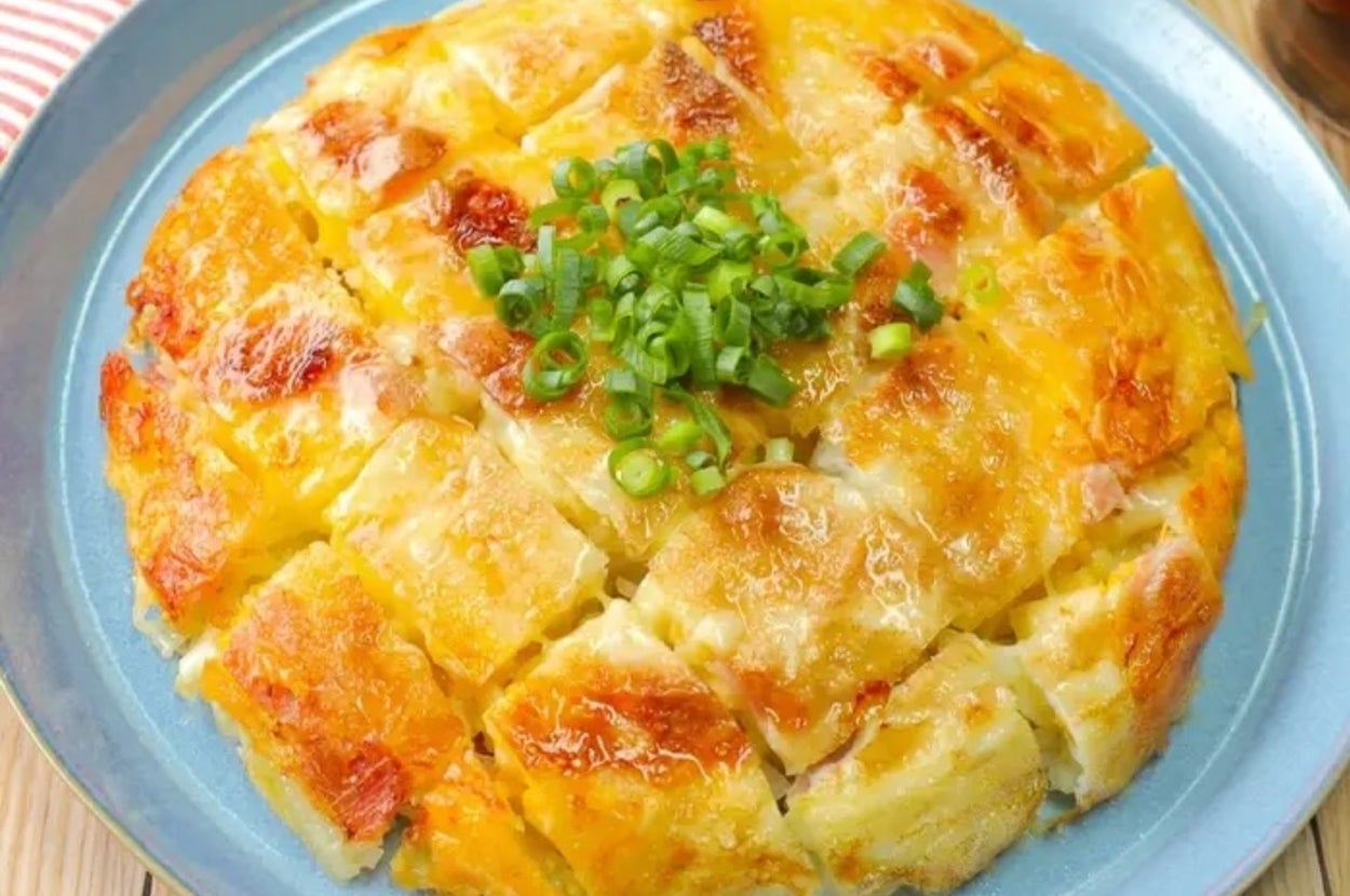 おいしそうなチーズがかかったパンケーキが青い皿に盛られている。上に刻んだネギが載っている。