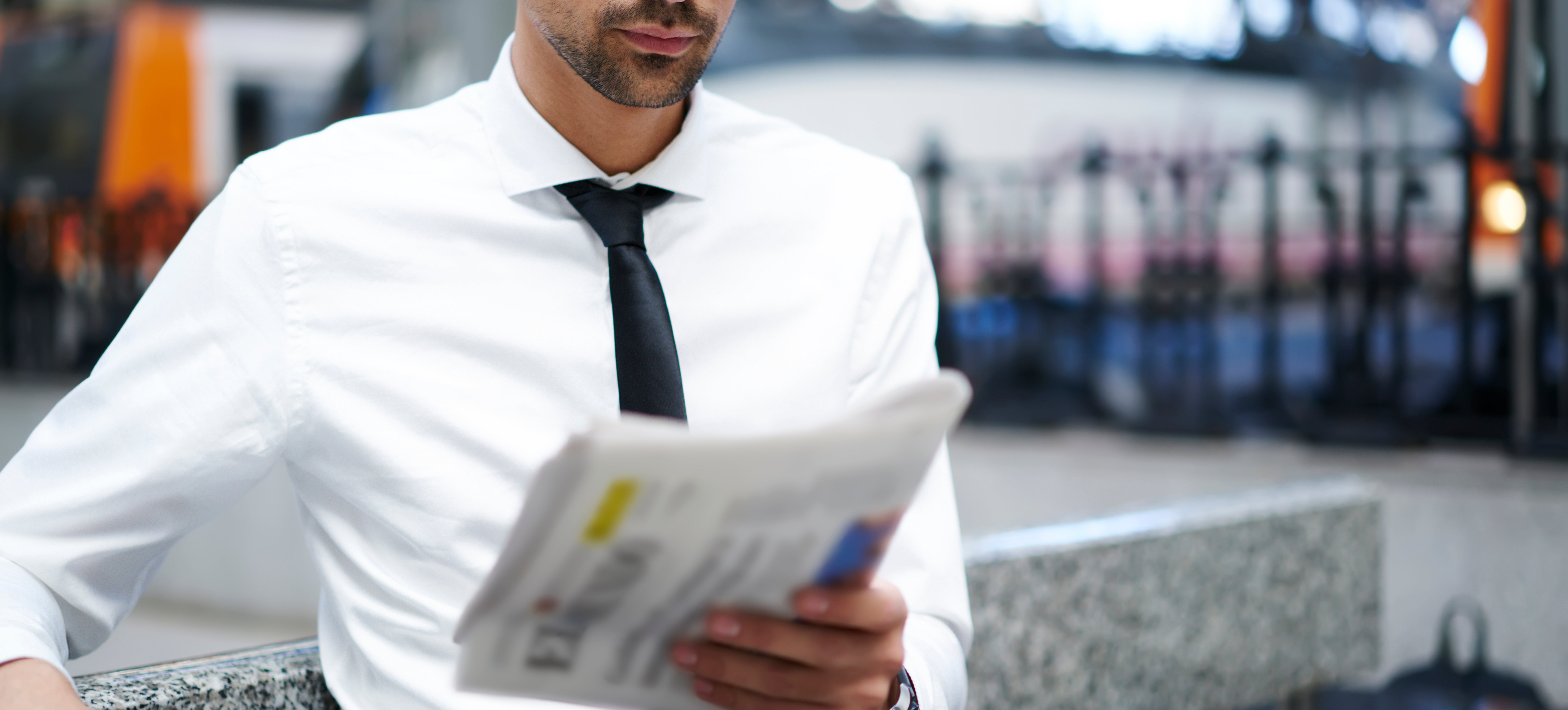Man successful  ceremonial  attire reads a paper  astatine  a bid     station, with a focused expression