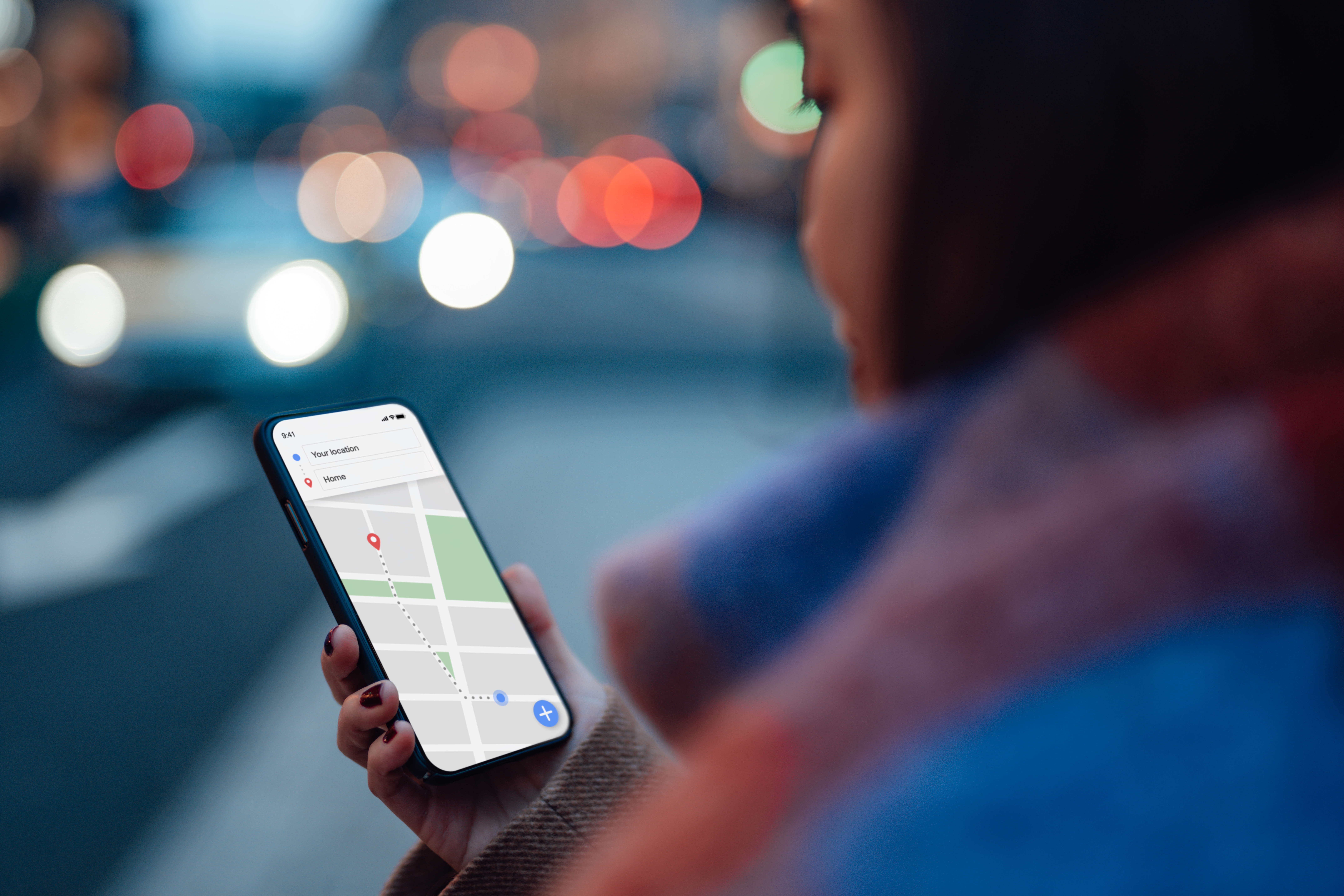 Person using a smartphone with a map app in a city setting, cars and streetlights blurred in the background
