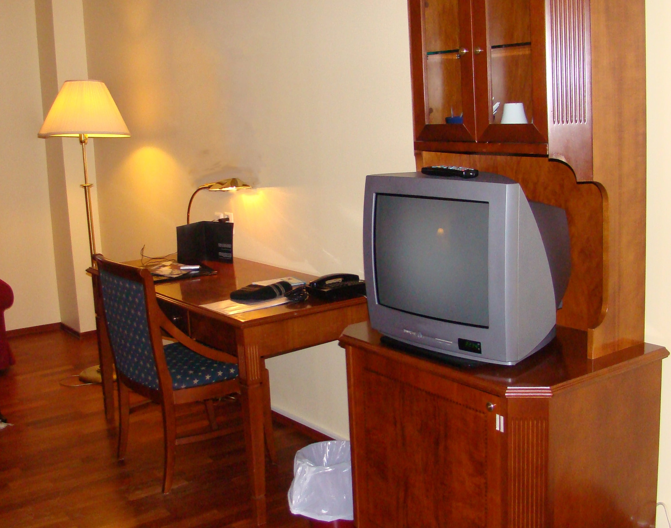 Hotel country   with woody  TV stand, older exemplary  TV, desk, chair, table  lamp, and a fewer  scattered items connected  the level  and desk