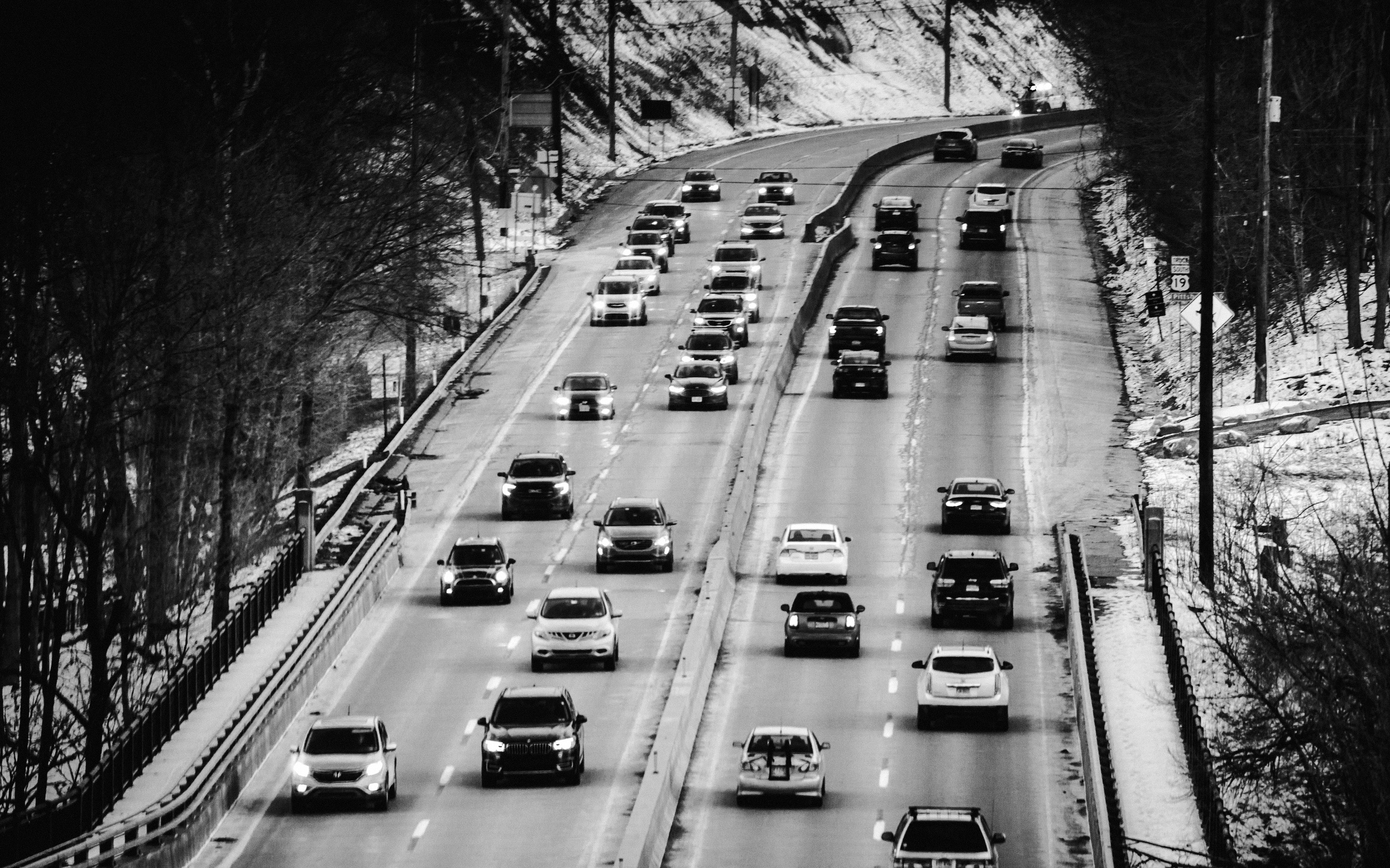 Cars question   connected  a multi-lane road  flanked by trees successful  a wintertime  setting. Traffic flows steadily, with disposable   snowfall  connected  the ground