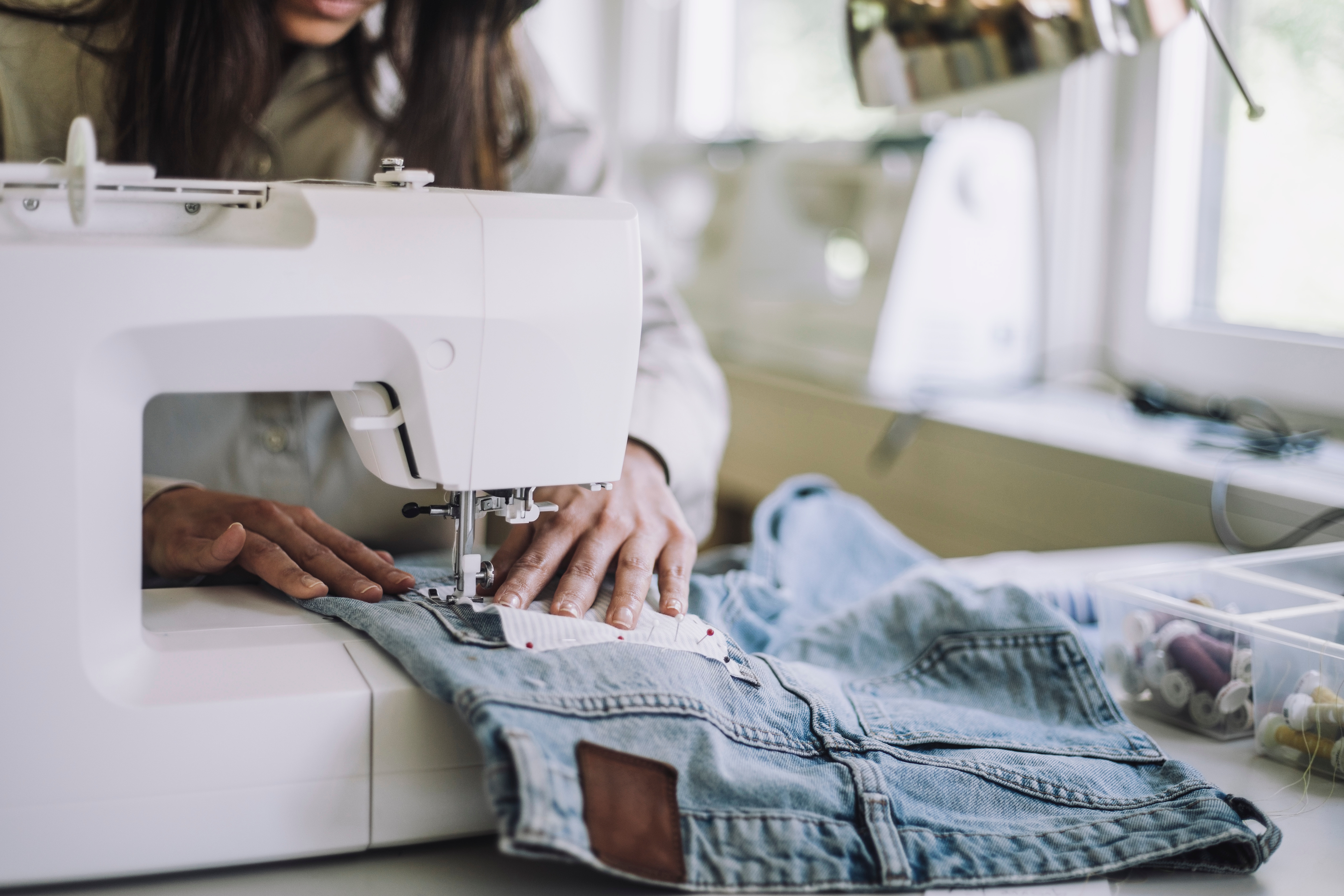 Person sewing denim cloth  connected  a sewing machine, with absorption   connected  their hands guiding the material