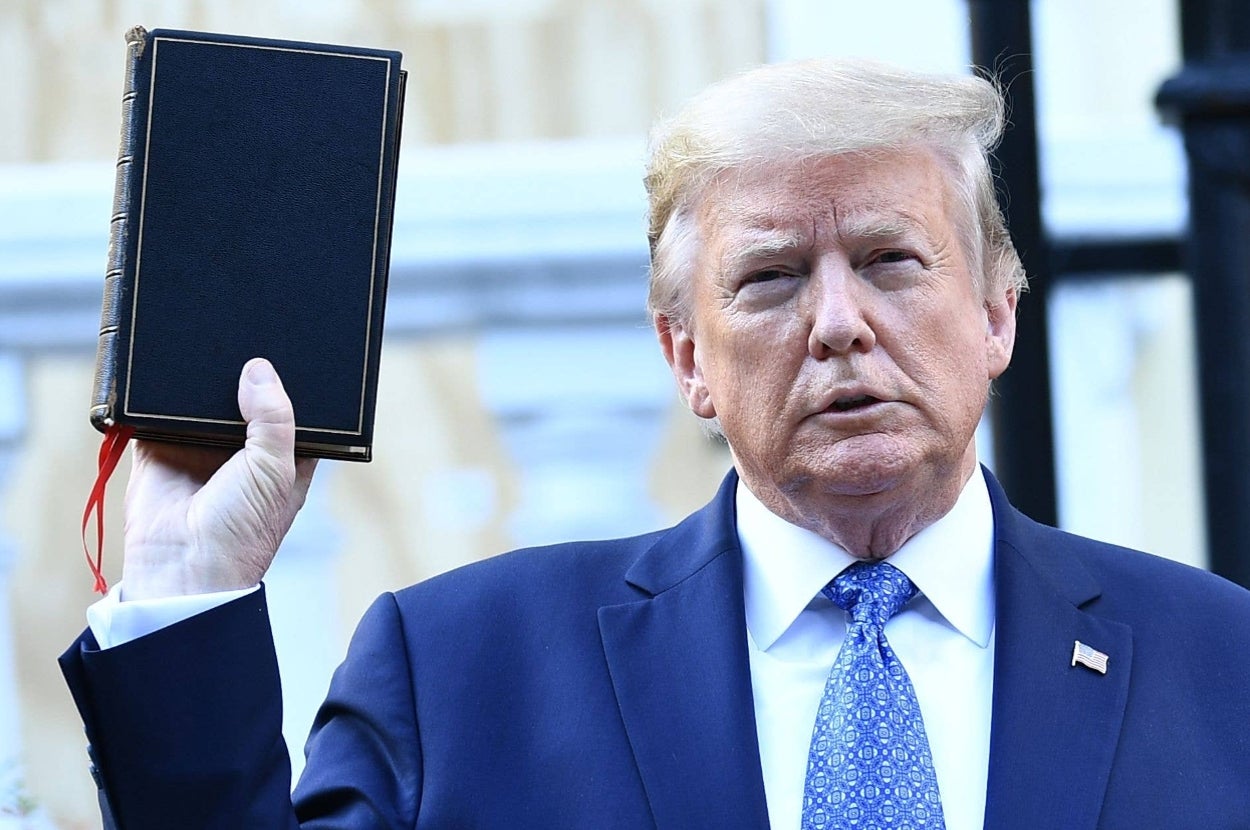 Person in a suit holds up a book during a public appearance