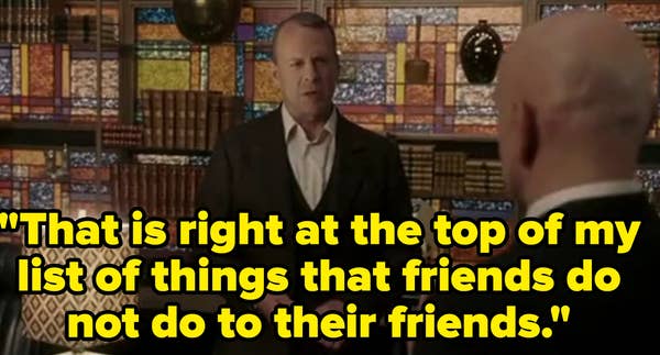 Two people in a study-like room with a stained glass wall and books. One person is wearing a suit