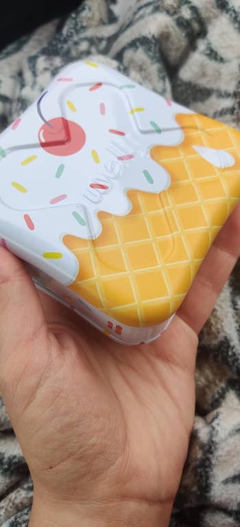 Hand holds a waffle-inspired tiny instrumentality with an crystal pick plan connected the lid, featuring a cherry and colorful sprinkles