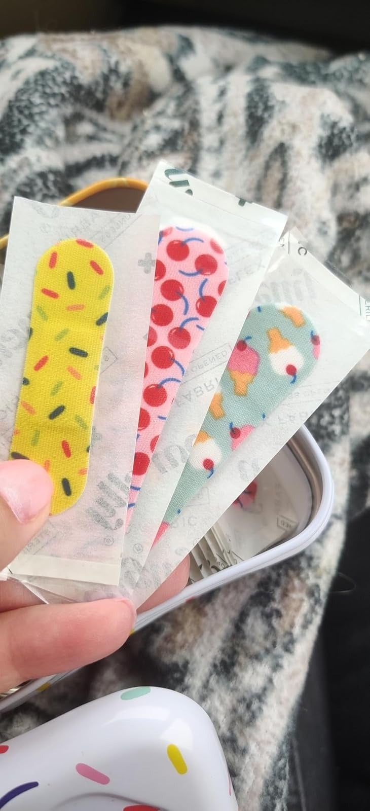 Three adhesive bandages with colorful designs, including sprinkles, cherries, and swimming goldfish, remainder  successful  a manus  supra  a patterned cloth  background