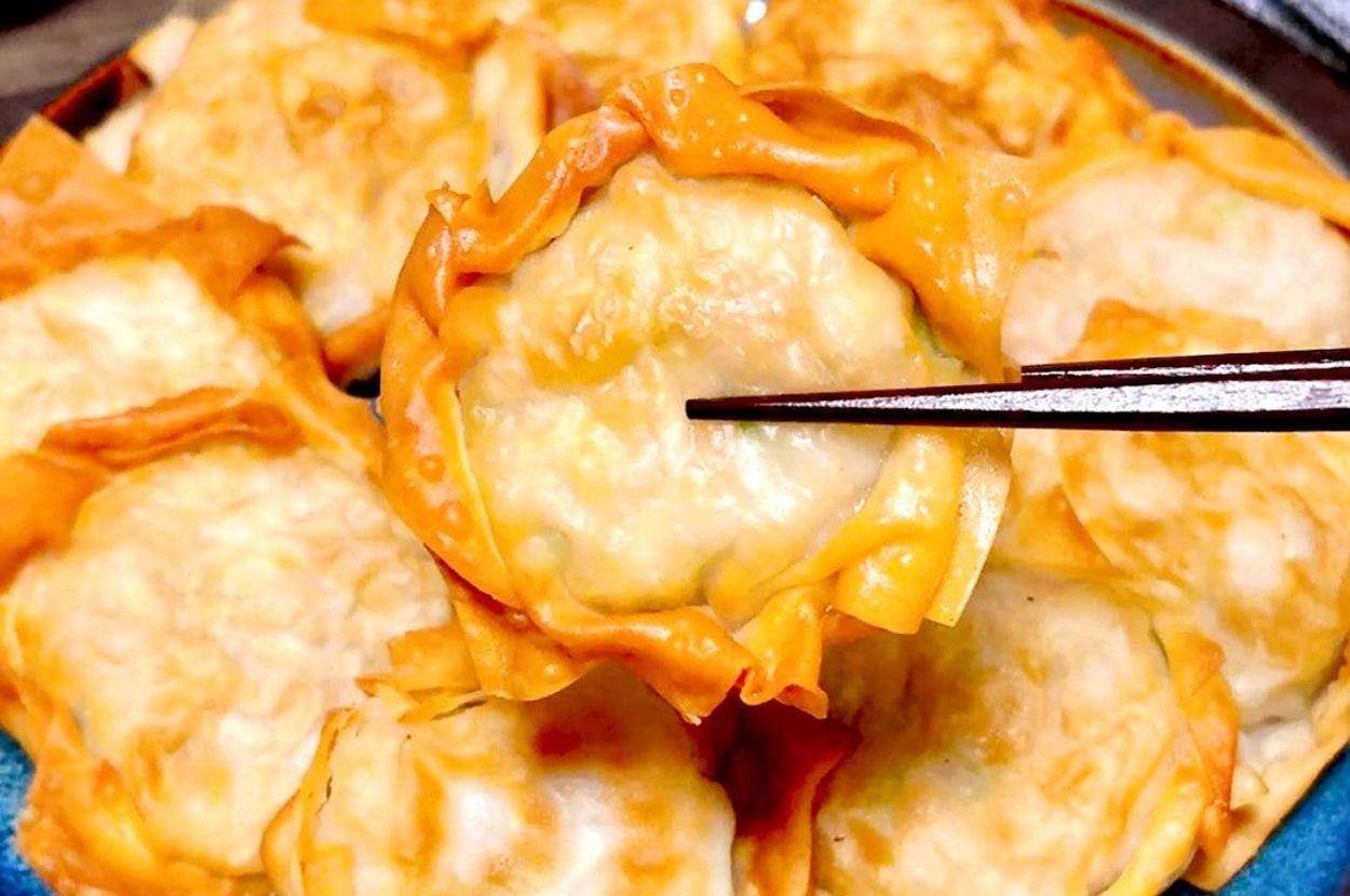 お皿に盛られた焼き餃子を箸で持ち上げている様子。