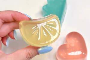 レモン形のゼリーを持つ手、背景にハートとケーキ形のゼリー。