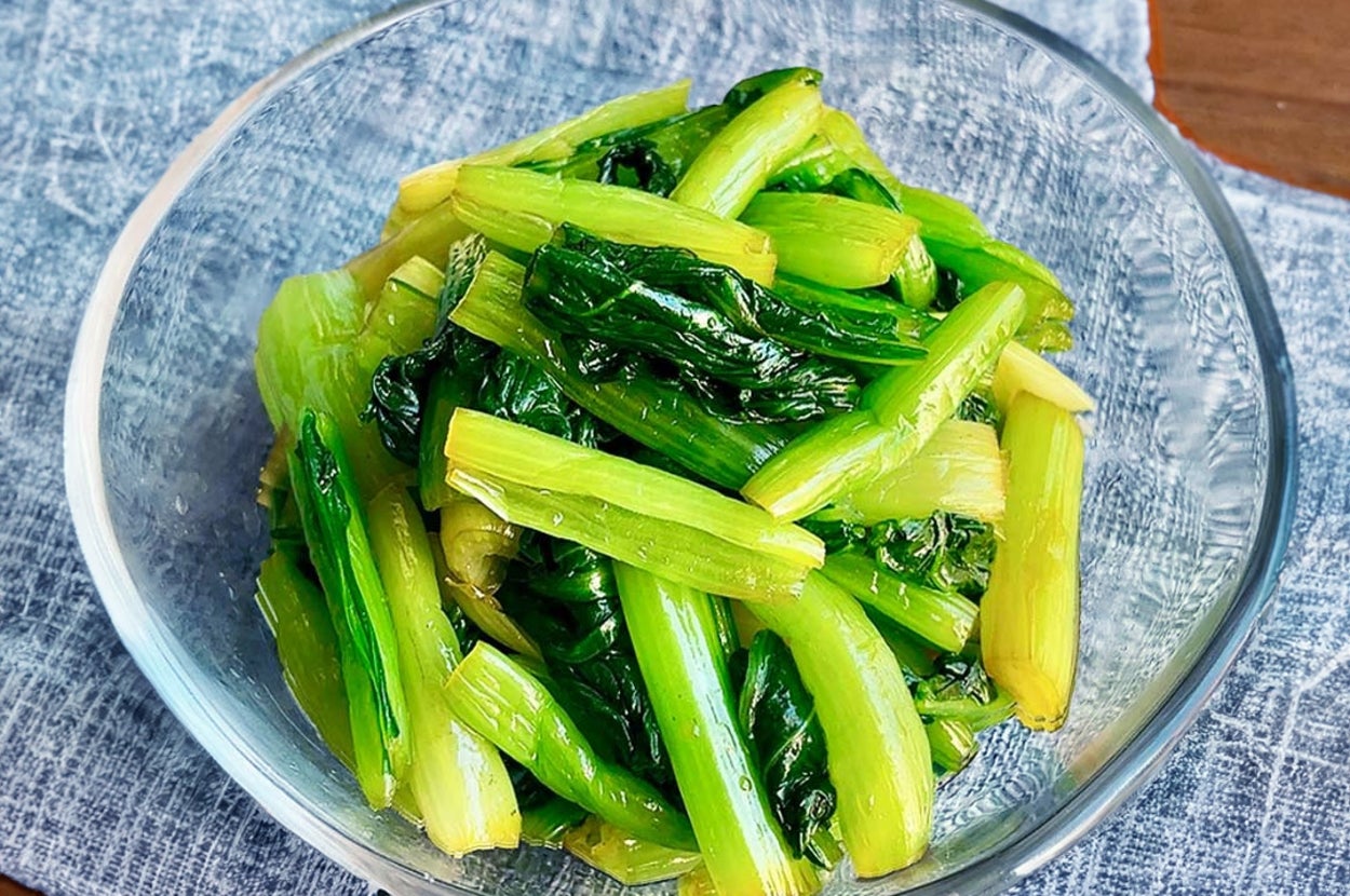 ガラスのボウルに盛られた新鮮な青菜の炒め物が、青い布の上のテーブルに置かれている。