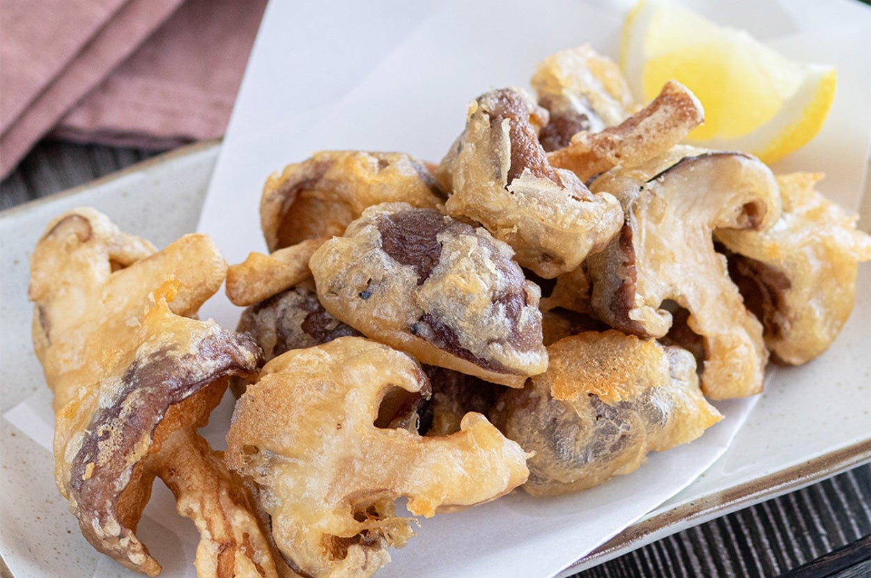 揚げたしいたけの天ぷらが皿に盛られている。レモンのくし切りが添えられている。