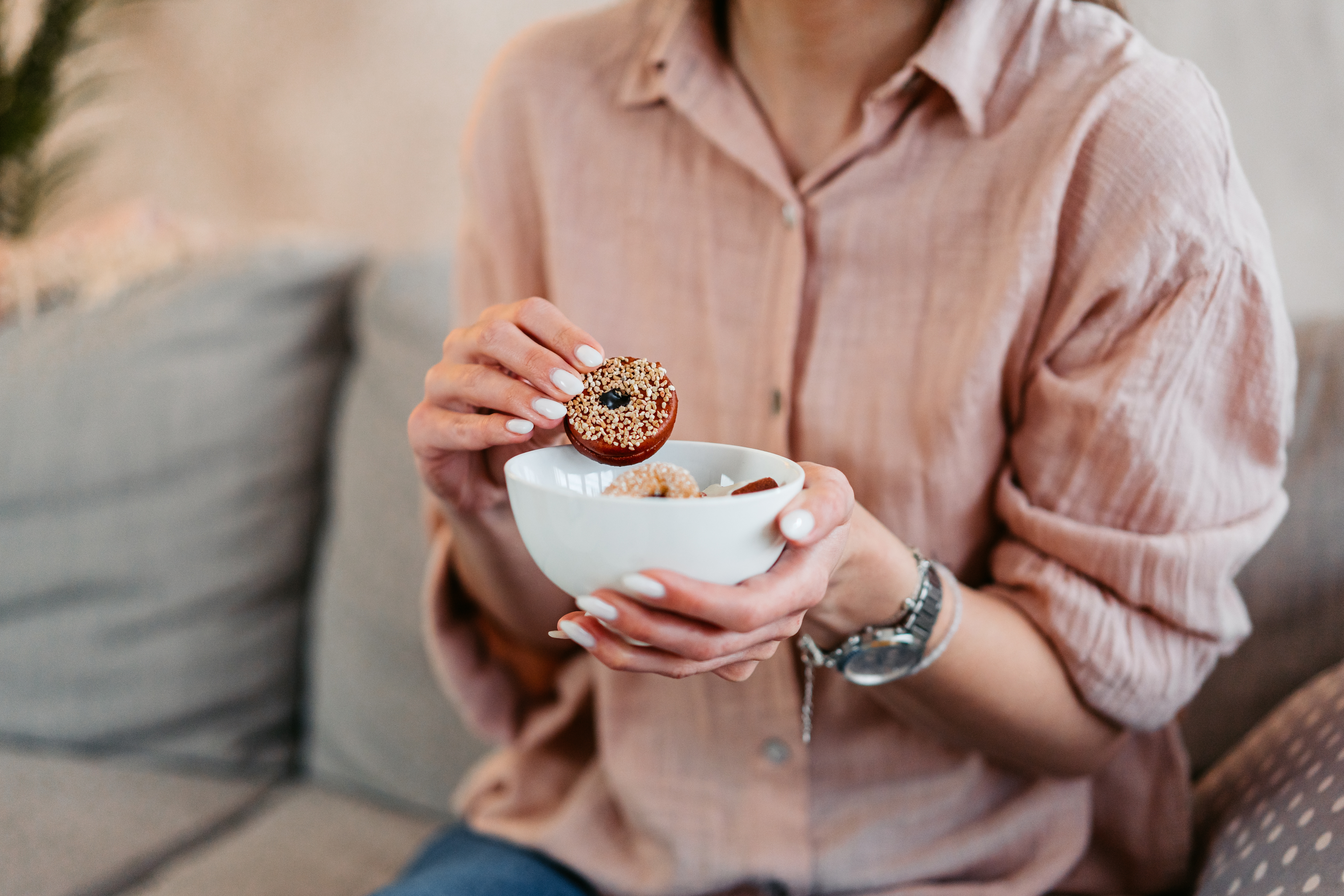 Person i uformelt antrekk sitter, holder en bolle med granola og legger en smultringformet gjenstand på toppen, noe som foreslår en rask frokost eller snacks