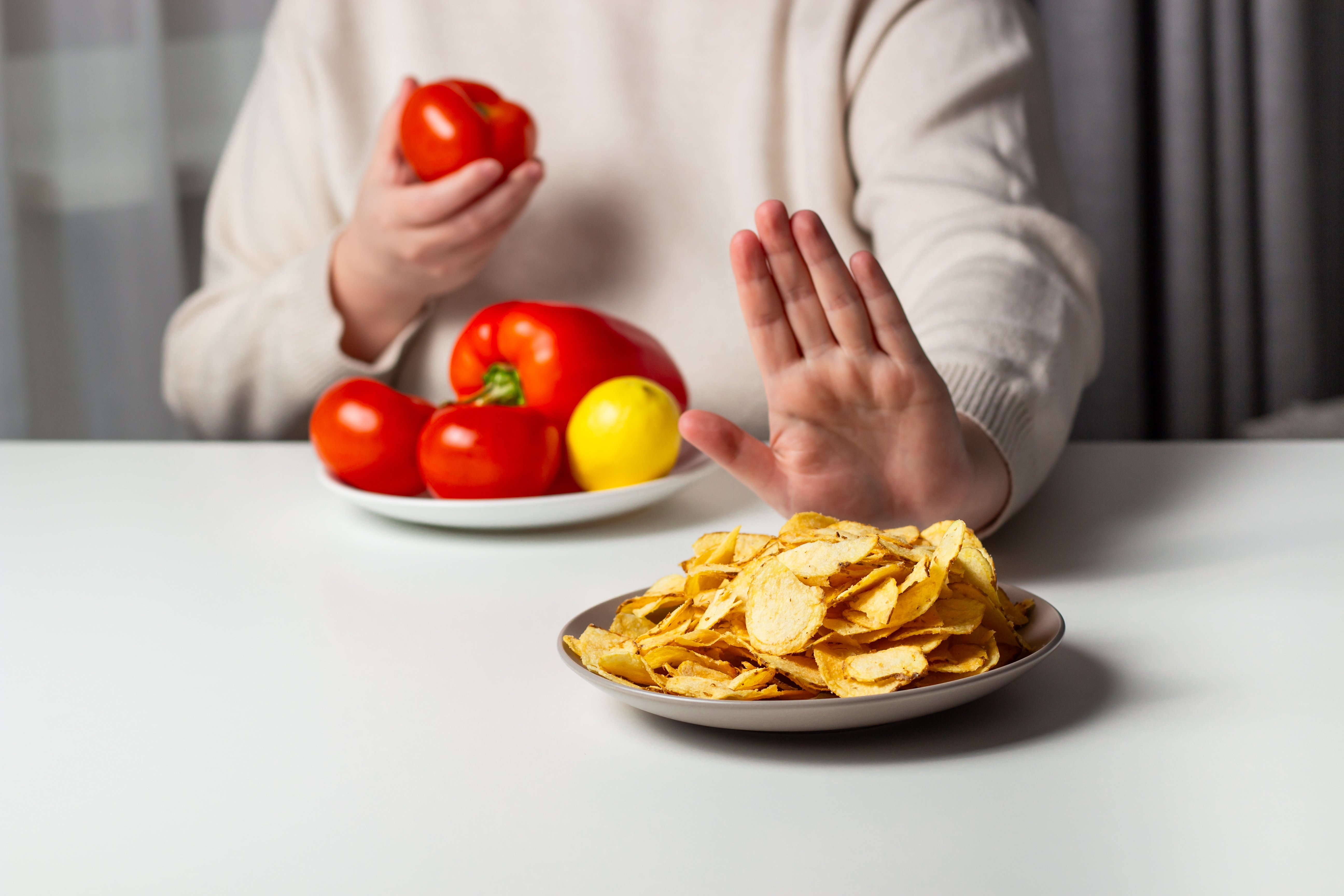 Person som nekter en tallerken chips med en utstrakt hånd mens han holder en bolle med ferske grønnsaker, inkludert tomater og en sitron
