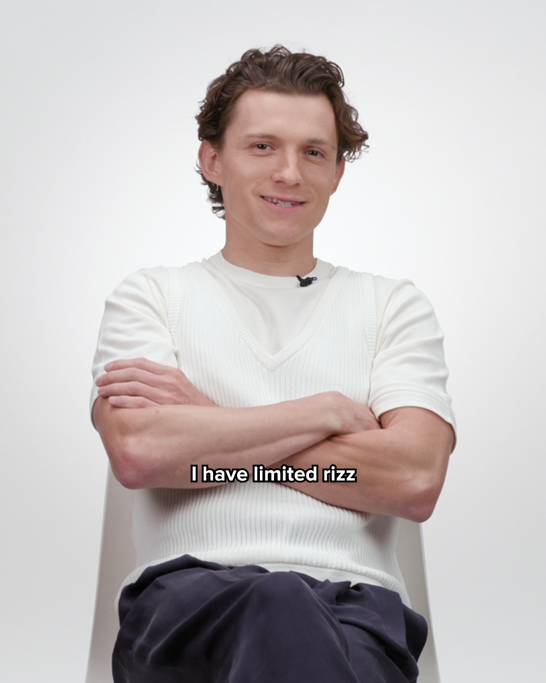 Person som sitter med armene i kors, iført en hvit kortermet genser over en skjorte, smiler til kameraet. Tekst på bildet lyder: