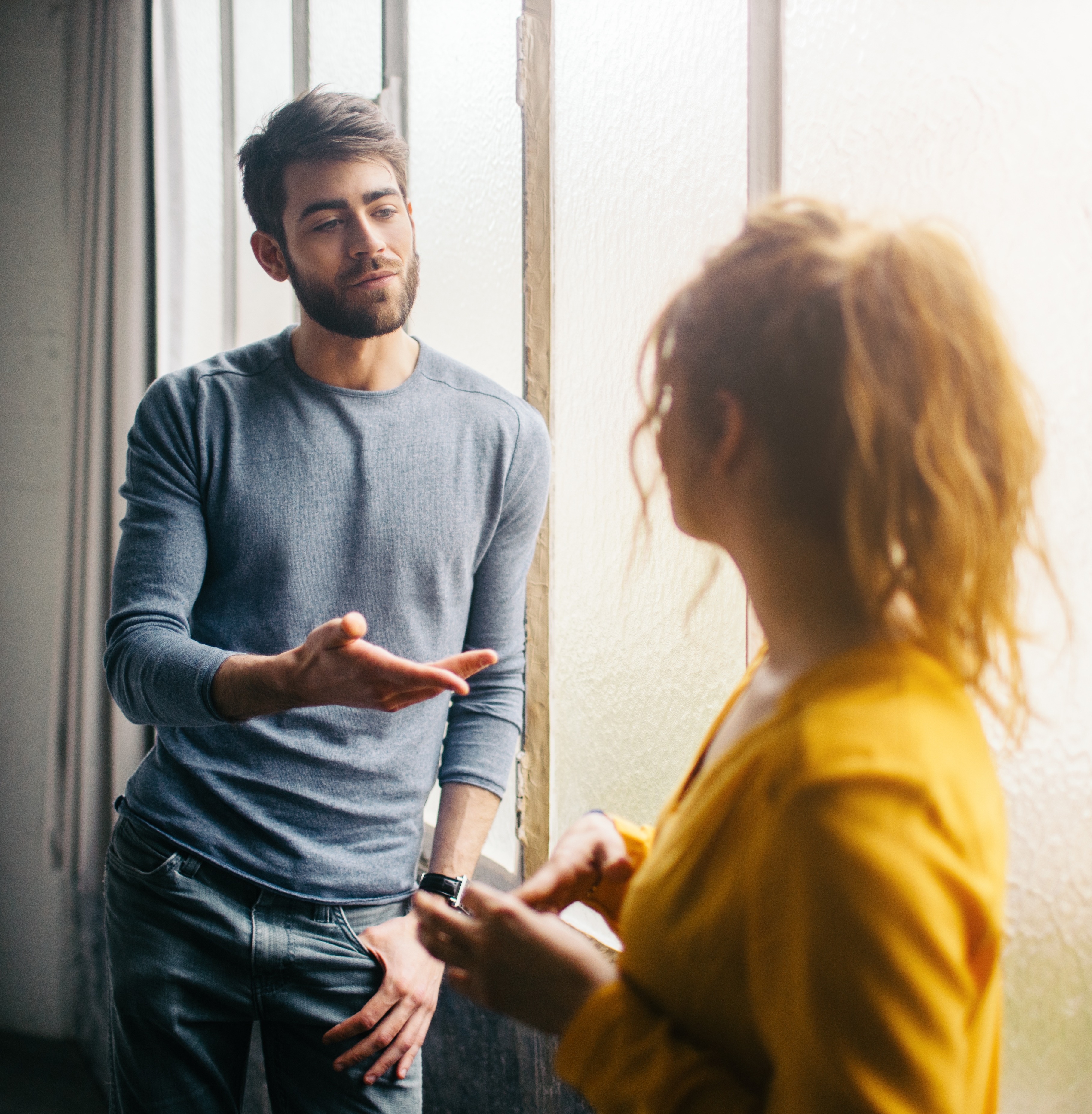 To personer snakker tilfeldig nær et solbelyst vindu. Mannen gestikulerer mens kvinnen lytter oppmerksomt