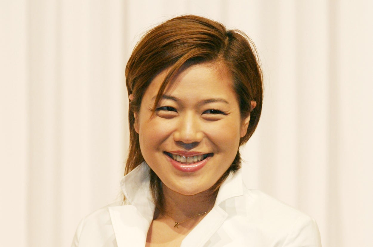 女性が白いジャケットを着て笑顔で立っている。