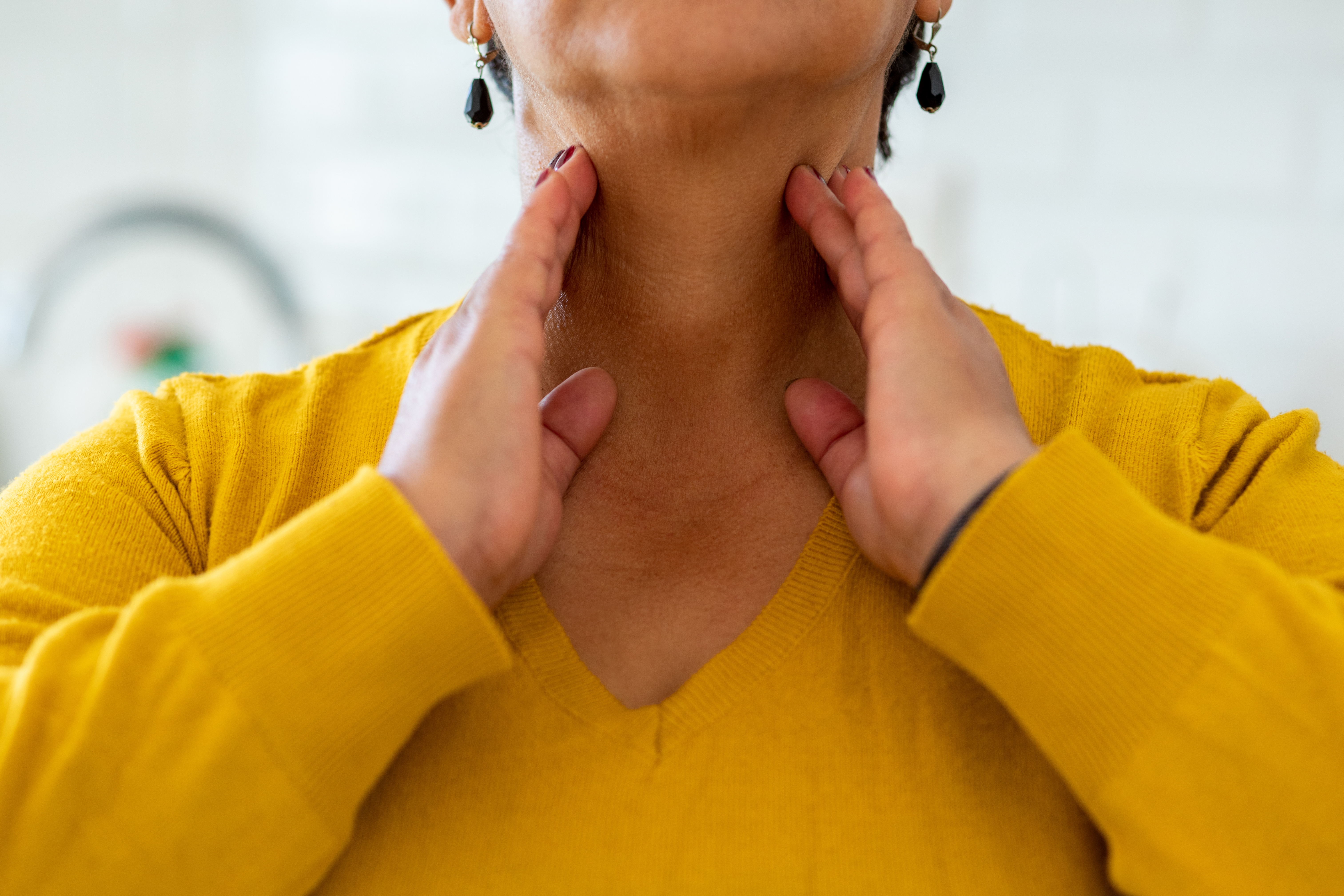 Person gently massaging their neck with both hands, wearing a V-neck sweater and earrings