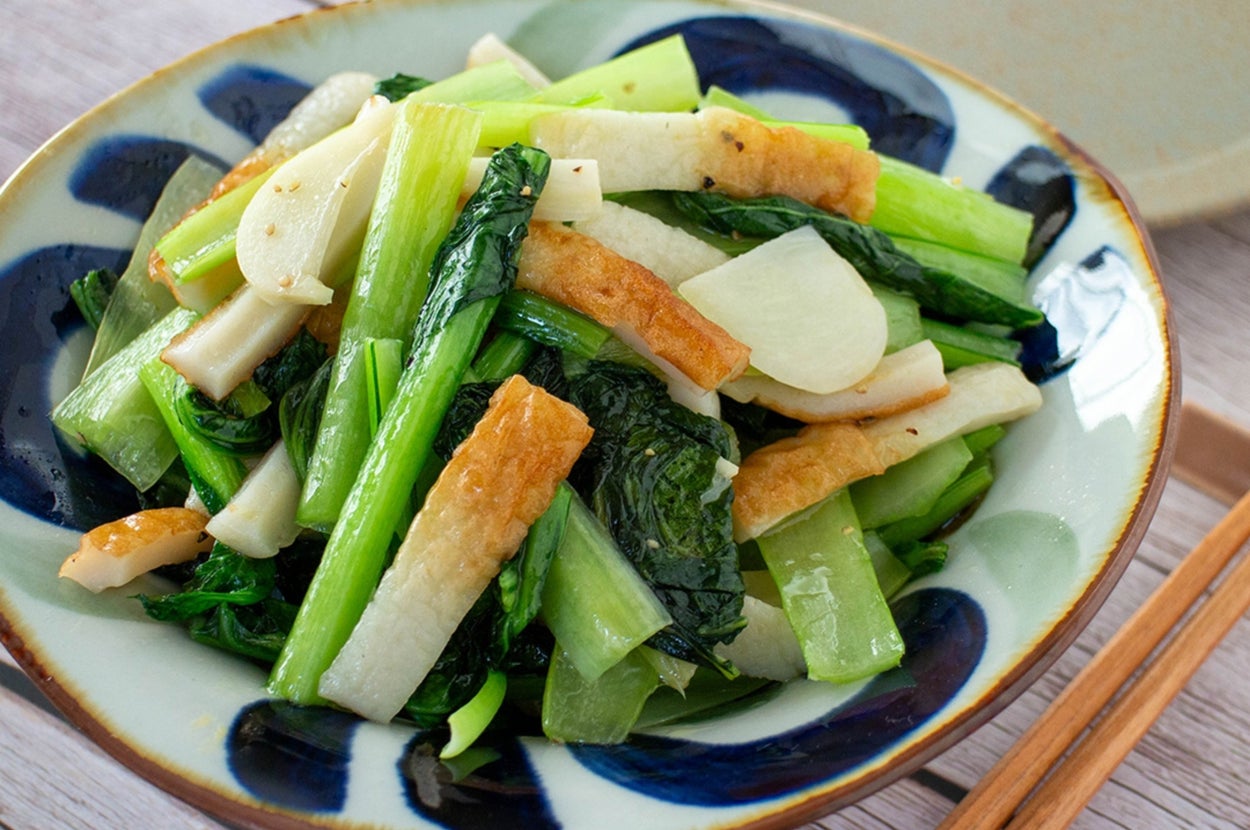 大皿に盛られた大根と青菜の炒め物。テーブルには箸が置かれている。