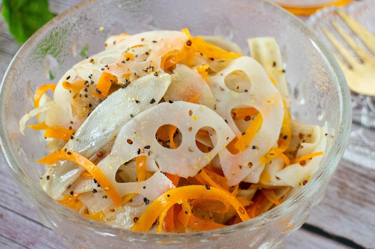 レンコンと人参のサラダがガラスのボウルに盛られている。背景に小瓶のはちみつが見える。