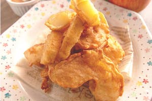 リンゴの天ぷらが皿に盛られており、バックにはリンゴとディップソースが見える。